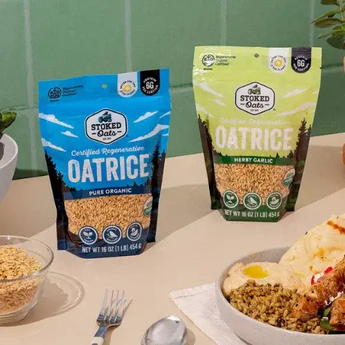 Two packages of Stoked Oats oatrice on a table with a bowl of food and utensils.