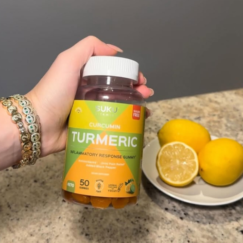 Person holding a bottle of Suku vitamins tumeric in front of a speckled counter with a plate of lemons nearby