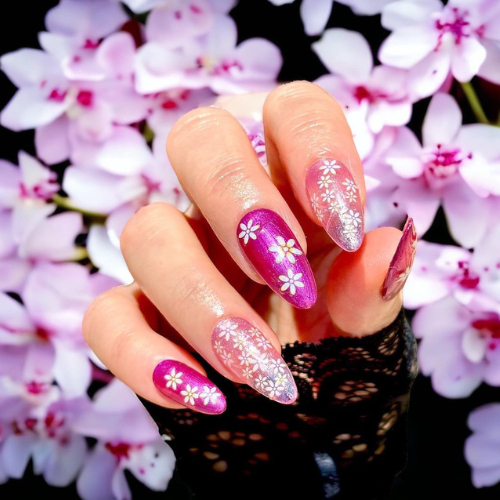 Hand with nails painted pink with cherry blossoms in the background