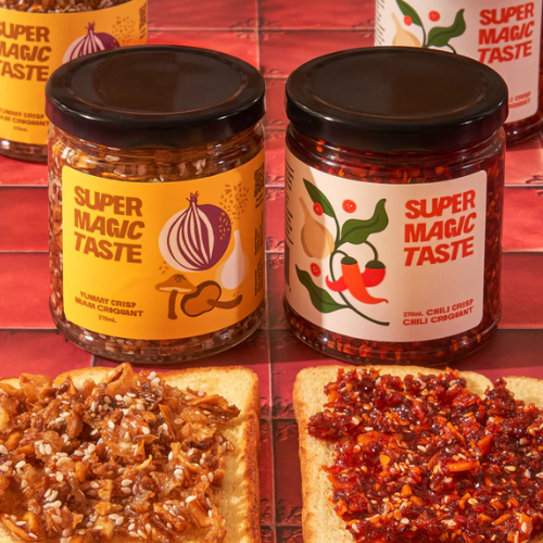 Two jars of 'Super Magic Taste' condiment on a red background with bread slices topped with the condiment.