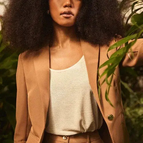 Woman in beige blazer and white top among green foliage
