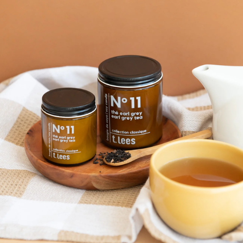 Two jars of t. lees tea on a wooden tray with a cup of tea and teapot.
