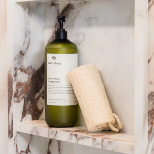 Green bottle of 'BathShop' soap on a marble shelf with a loofah.