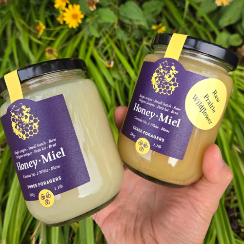 Two jars of honey labelled 'Honey Miel' held in a hand with a natural background.