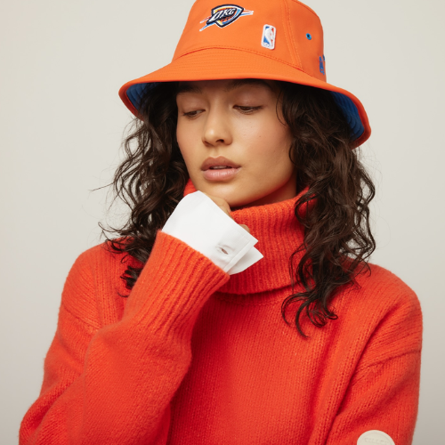 Person wearing an orange bucket hat and sweater with a visible brand logo.