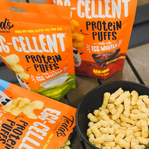 Egg-Cellent Protein Puffs packaging with a bowl of puffs on a table.