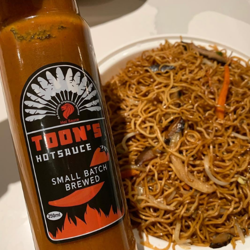 Bottle of Toon's Hot Sauce next to a bowl of noodles