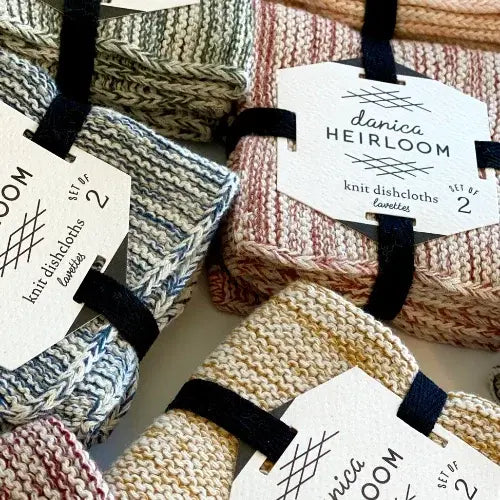 Knitted dishcloths with tags labeled 'danica Heirloom' on a textured surface.