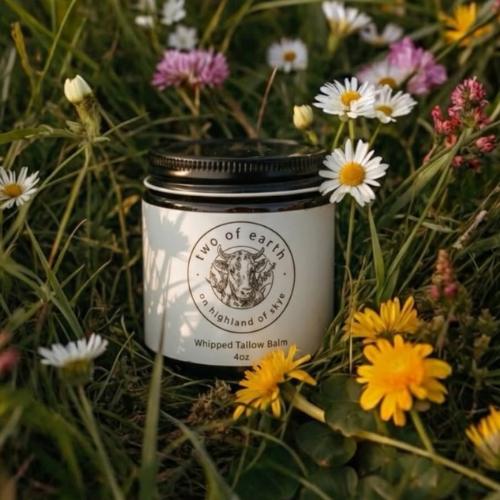 Jar of 'Two of Earth' balm surrounded by flowers in a natural setting