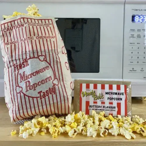 Two bags of microwave popcorn with popcorn scattered on a wooden surface in front of a microwave.