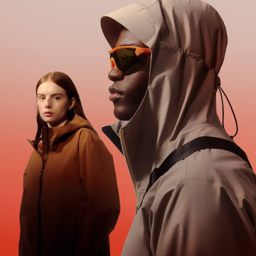 Two people wearing hooded jackets against a gradient background