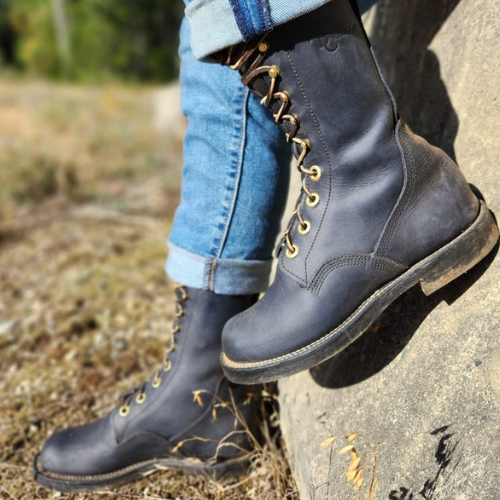 Person wearing gray leather boots with gold laces on a natural background