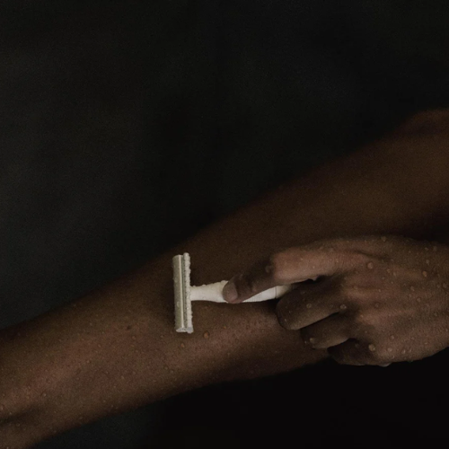 Person shaving leg with white razor in front of dark background