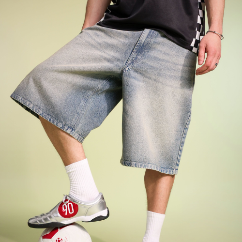 Person wearing light blue denim shorts and white sneakers on a plain background