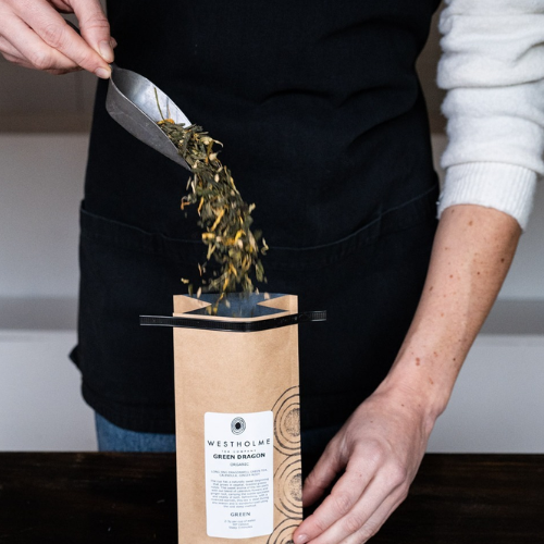 Person pouring tea leaves into a Westholme Green Dragon tea package.