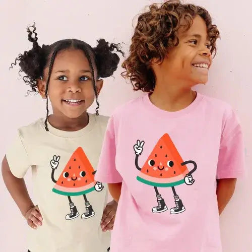 Two children wearing Whistle & Flute t-shirts with cartoon watermelon designs on a light pink background