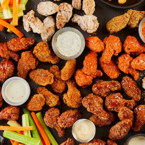Assorted fried chicken wings with dipping sauces and vegetables on a black surface