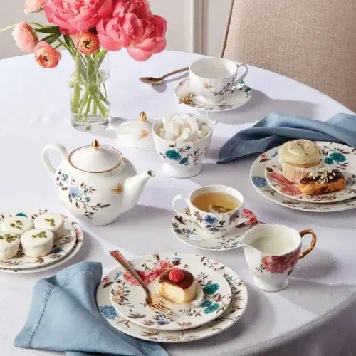 Tea set with teapot, cups, saucers, and pastries on a table with pink flowers.