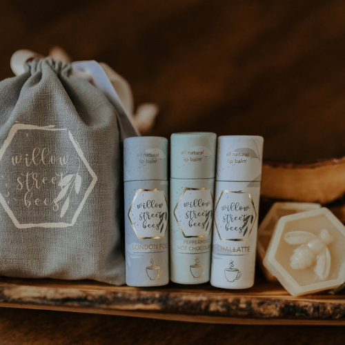 Set of willow street bees lip balm containers with a branded drawstring bag on a wooden surface.