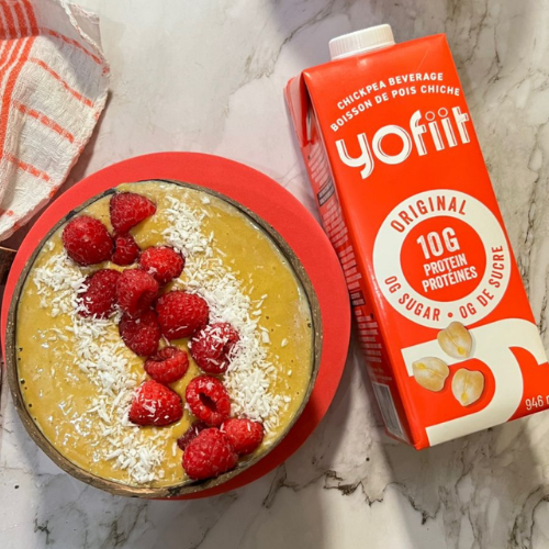 Yofit chickpea beverage carton next to a bowl of smoothie with raspberries on a marble surface