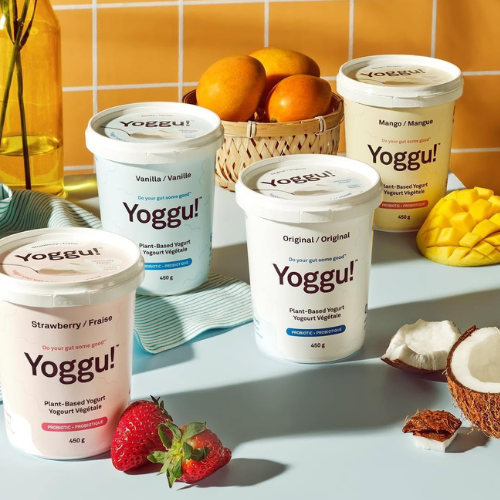 Yoggu plant-based yogurt containers on a table with fruits and a basket in the background.